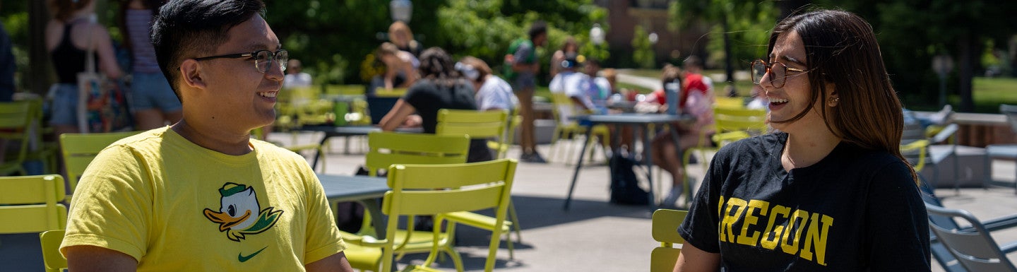 students sitting at table outside EMU Fishbowl wearing Ducks gear